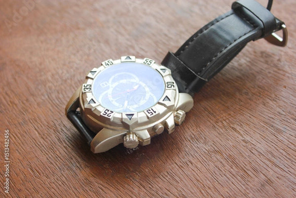 Fototapeta Luxury analog wristwatch with a black leather strap and stainless steel bezel, placed on a wooden surface, showcasing bold numerals and a modern chronograph dial.
