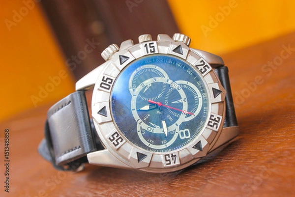 Fototapeta Luxury analog wristwatch with a black leather strap and stainless steel bezel, placed on a wooden surface, showcasing bold numerals and a modern chronograph dial.