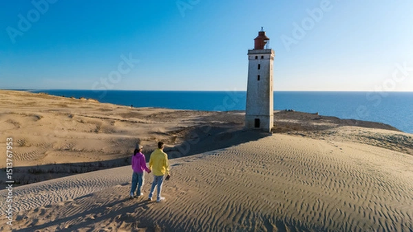 Fototapeta Couple explores the iconic lighthouse on the sandy shores of Denmark during a serene day