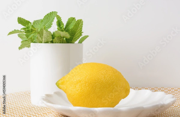 Obraz Lemon lying on a saucer on a light background with mint leaves in a white mug, selective focus