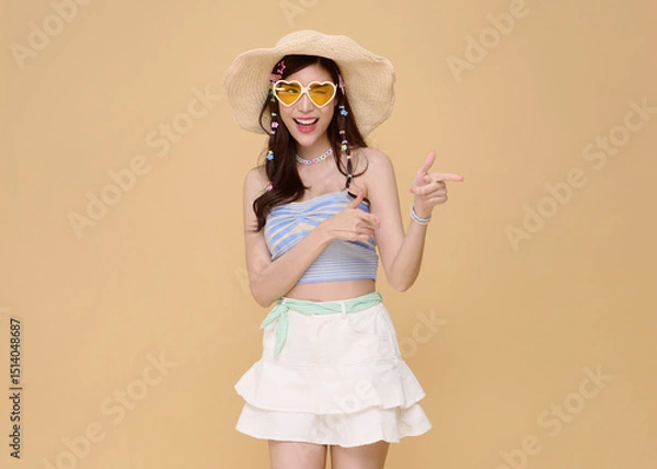 Fototapeta Happy Young beautiful Asian woman dressed in summer clothes smiling and pointing to empty copy space isolated on nude color background.