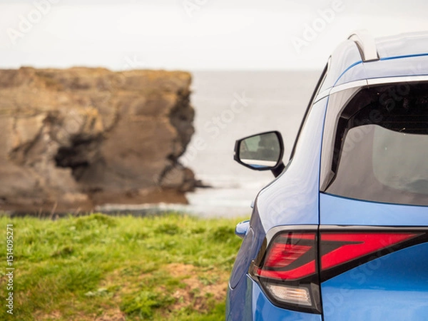 Fototapeta A blue car is parked on the side of a road next to a cliff overlooking the ocean. Travel and tourism. Trip to nature, cloudy day, rough stone coast. Sightseeing landmarks. West of Ireland.