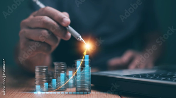 Fototapeta Business analytics and financial concept. Saving money for future growth. Businessman using pen pointing to analyze financial graph for investment, Stack of coins and laptop. Financial planning.