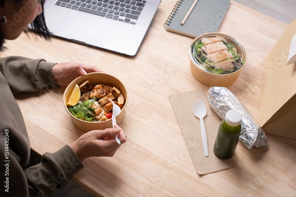Fototapeta Asian woman eating healthy meal while working, Businesswoman having a lunch break at the office