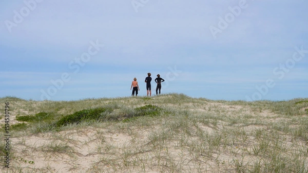 Fototapeta Surfers in Australia looking out at the ocean from behind.People standing on a sandy dune overlooking the ocean during a calm day at the beach
