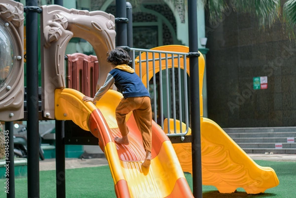 Obraz Happy child sliding down a colorful playground slide on a sunny day. Outdoor fun, childhood joy, and active play in a safe, urban recreational space.