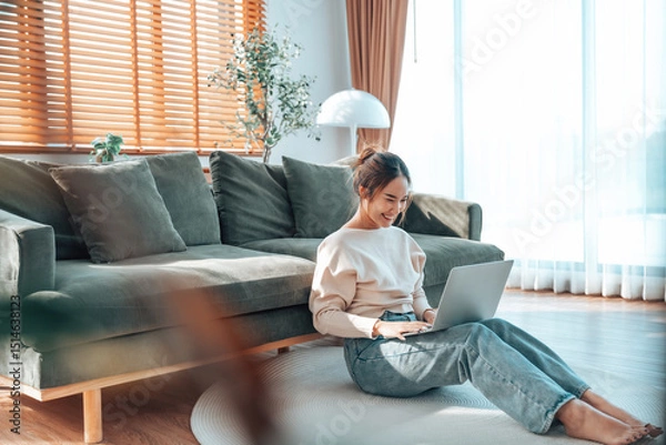 Fototapeta Young Asian beautiful woman relaxing on comfortable couch, using laptop at home, happy girl chatting with friends in social network, spending weekend, watching movie, shopping online