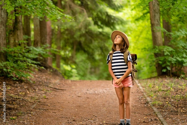 Obraz Young adventurer with backpack gazing upward during sunny forest hike. Joyful outdoor activity connecting with nature during summer break.