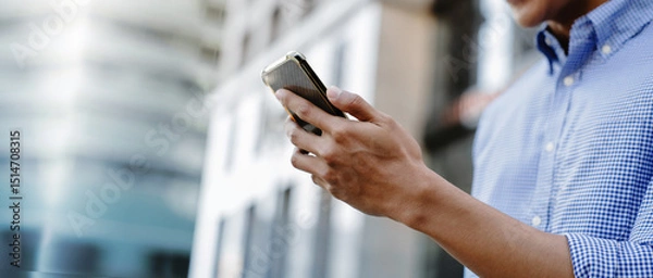 Fototapeta A man using a smartphone in an urban environment, representing mobile communication, digital lifestyle, and business on the go