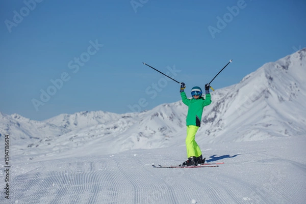 Obraz Skier in neon green jacket lifts poles overhead on sunlit slope