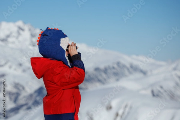 Obraz Boy with binoculars surveys snowy mountain scenery in binocular