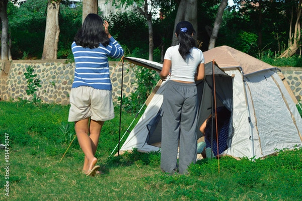 Fototapeta One girl begins entering the tent while two others observe and check the structural stability from outside to ensure everything is in place.