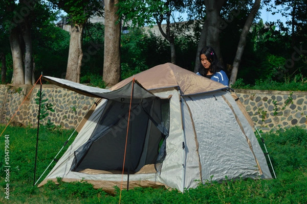 Fototapeta A single girl is focused on the back side of the tent, making final adjustments to ensure the structure is stable and weather-ready.