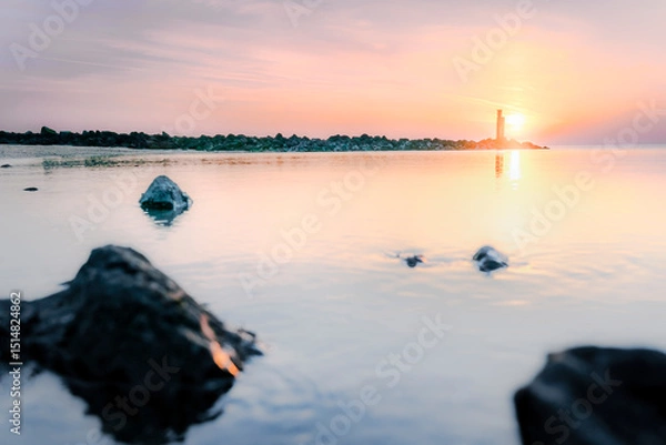 Fototapeta Serene Sunrise at the Coast with Distant Lightsignal
