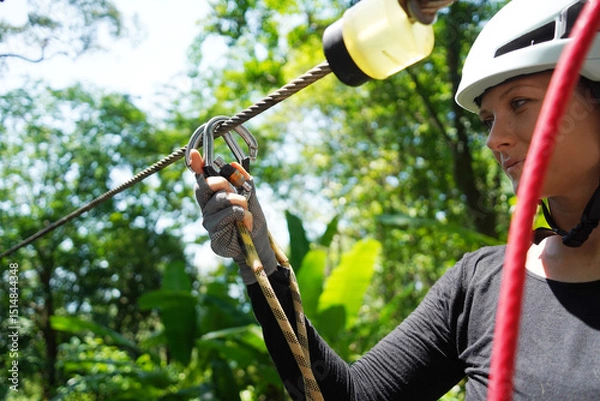 Fototapeta Woman is enjoying an exhilarating ride on a zip line that traverses the thick woods surrounding her