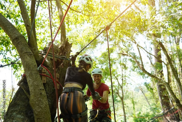 Fototapeta A man and a woman is walking across a challenging ropes course in the extreme park