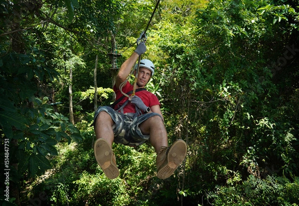 Fototapeta A man is enjoying an exhilarating ride on a zip line that traverses the thick woods surrounding him
