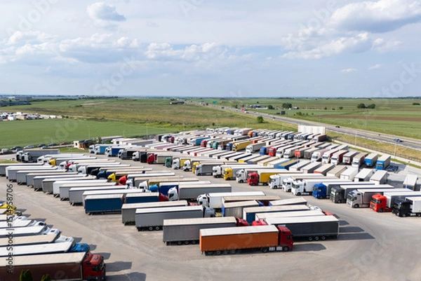 Fototapeta Aerial view of a large truck parking lot at a logistics hub, with multiple commercial semi trucks parked in organized rows.