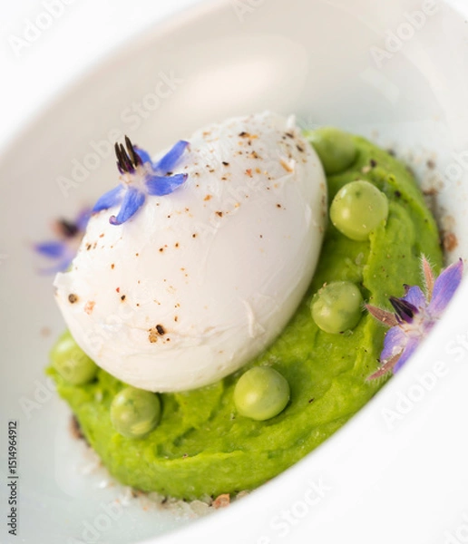 Obraz A fresh pea puree is beautifully plated, featuring a poached egg at the center and adorned with borage flowers. The dish showcases vibrant colors and textures, perfect for any spring menu.