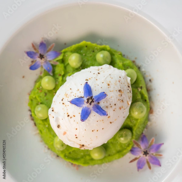 Obraz A fresh pea puree is beautifully plated, featuring a poached egg at the center and adorned with borage flowers. The dish showcases vibrant colors and textures, perfect for any spring menu.