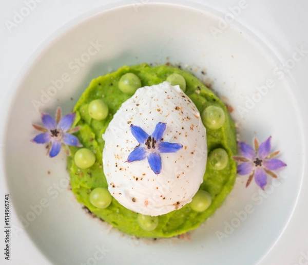 Obraz A fresh pea puree is beautifully plated, featuring a poached egg at the center and adorned with borage flowers. The dish showcases vibrant colors and textures, perfect for any spring menu.