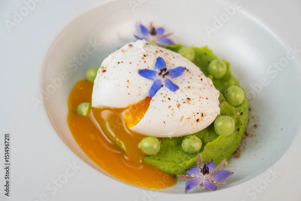 Obraz A fresh pea puree is beautifully plated, featuring a poached egg at the center and adorned with borage flowers. The dish showcases vibrant colors and textures, perfect for any spring menu.