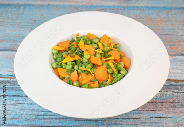 Obraz Fresh garden peas and carrots are cooked with salted butter, then garnished with chives and bright marigold flowers for an appealing and colorful side dish.