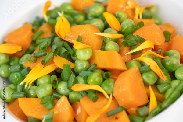 Obraz Fresh garden peas and carrots are cooked with salted butter, then garnished with chives and bright marigold flowers for an appealing and colorful side dish.
