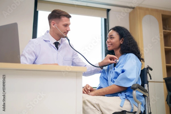 Obraz caucasian doctor in white gown using stethoscope to listen heart beat an afro hair woman client in examine room at hospital