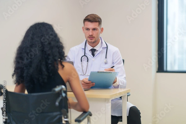 Obraz doctor in white gown with stethoscope,asking a woman disabled person on wheelchair for present illness to diagnosis and treatment in the examine room