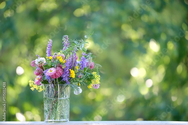 Fototapeta colorful meadow flowers in glass tumbler close up on table in garden, natural abstract background. Summer season. Beautiful floral composition.