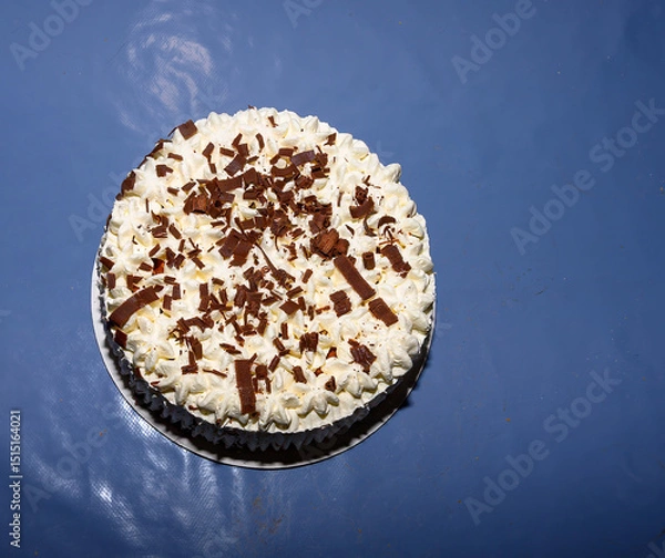 Obraz A beautifully decorated layered cream cake sits on a table with rich chocolate shavings on top. The cake features a smooth white frosting and an inviting appearance