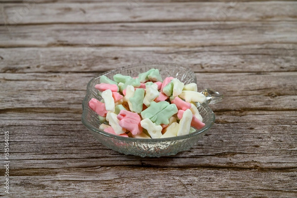 Obraz Brightly colored candy pieces in pastel shades are arranged in a crystal dish on a weathered wooden table. They create a cheerful and inviting display ideal for snacking or sharing
