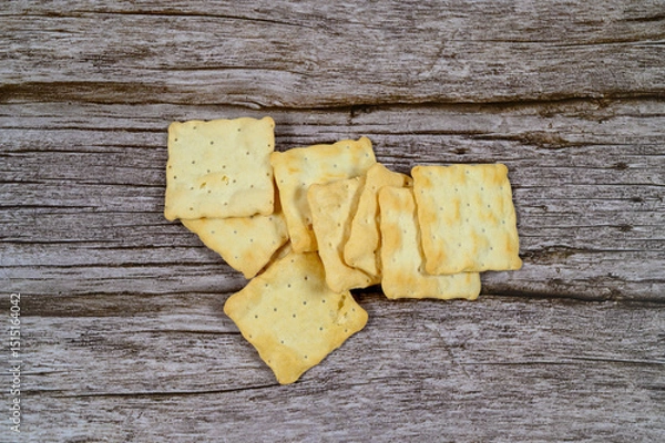 Obraz A pile of crispy, golden crackers rests on a weathered wooden table, perfect for enjoying with cheese or dips during a casual gathering or snack time