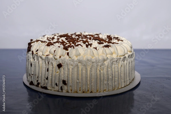Obraz A beautifully decorated layered cream cake sits on a table with rich chocolate shavings on top. The cake features a smooth white frosting and an inviting appearance