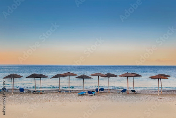 Fototapeta straw umbrella and sun loungers in line on a beach at sunset in Peloponnese Greece