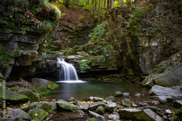 Obraz Waterfall in the heart of the Beskydy Mountains, surrounded by moss-covered rocks and lush forest. A long exposure captures the gentle flow of water falling into a tranquil pool in a secluded woodland
