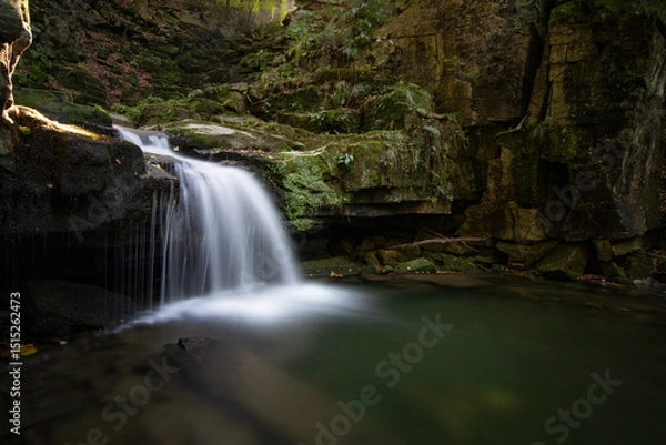 Obraz Waterfall in the heart of the Beskydy Mountains, surrounded by moss-covered rocks and lush forest. A long exposure captures the gentle flow of water falling into a tranquil pool in a secluded woodland