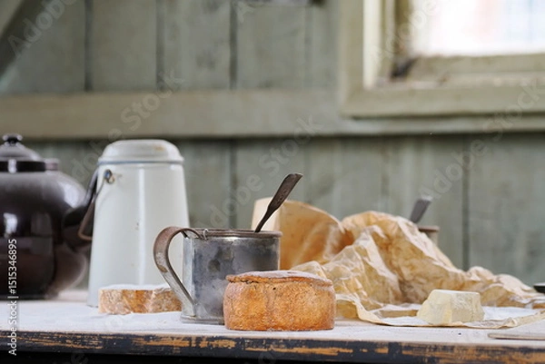 Fototapeta Rustic kitchen scene with bread, cheese and metal mugs, and vintage cookware on a flour-dusted table.
