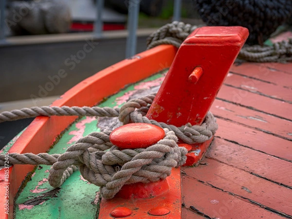 Fototapeta Close-up of a mooring rope tied to an red boat cleat on a vibrant painted deck.