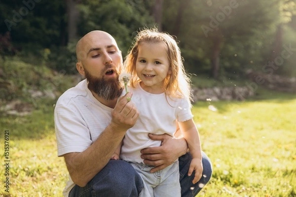 Obraz Father and daughter blowing dandelion in a park during a sunny day