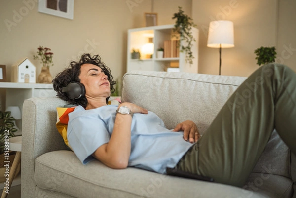 Obraz Mature woman lying on sofa with headphones and have guided meditation