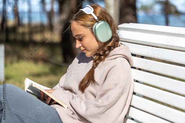 Obraz Teenage girl reading a book in the park sitting on a bench. Girl reading a book in the park.