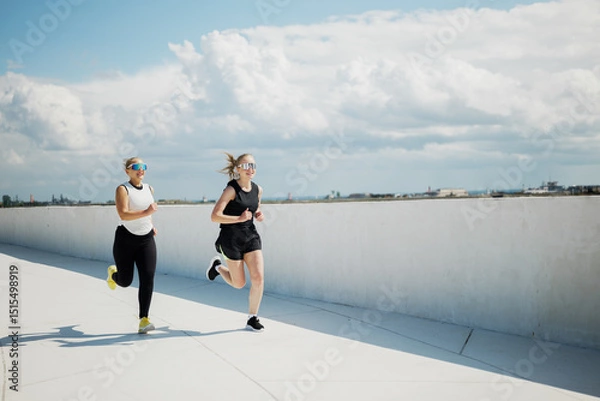 Obraz Two friends engage in an energetic morning run along a scenic waterfront path under a blue sky
