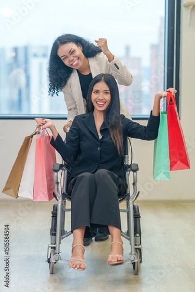 Obraz multiracial female friends with shopping bags in the urban building,a woman and a disability person on wheelchair enjoy shopping in the mall