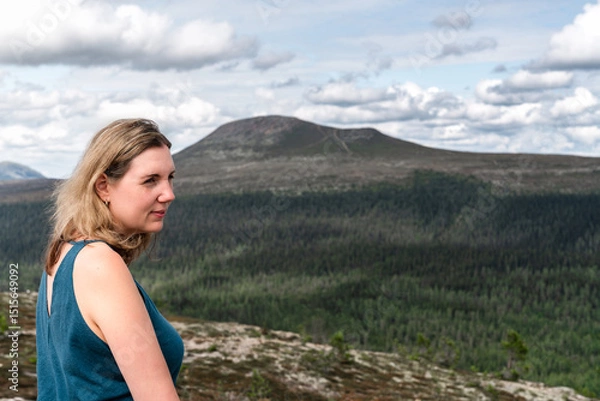 Fototapeta A woman stands on a mountain top, gazing away with the beautiful Städjan mountain visible in the background. In the serene landscape of Idre Dalarna Sweden