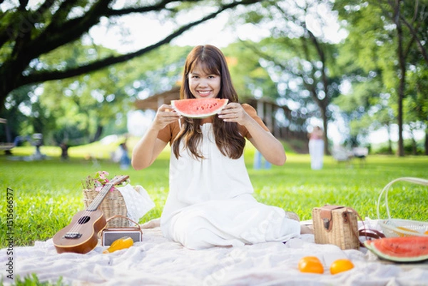 Obraz Family enjoys leisure picnic in green park where smiling woman holds slice of watermelon while people relax and share concept of outdoor fun and togetherness