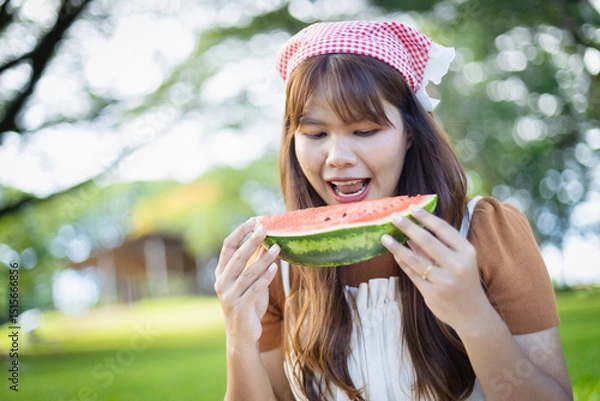 Obraz Young woman enjoys picnic outdoors holding slice of watermelon with joyful expression, capturing leisure and happy concept of people spending time with family