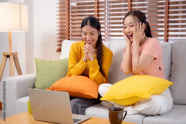 Obraz Two young asian woman sitting on sofa using laptop computer for video call in living room at home, female using social media on notebook for online and conversation distant, lifestyles concept.