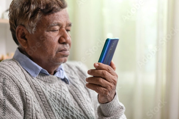 Fototapeta Sad elderly Asian man using mobile phone while sitting on sofa at home.